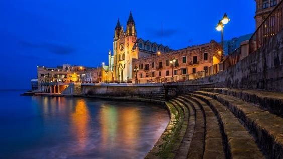 St Julian’s bay and its church lit up at dusk in Malta